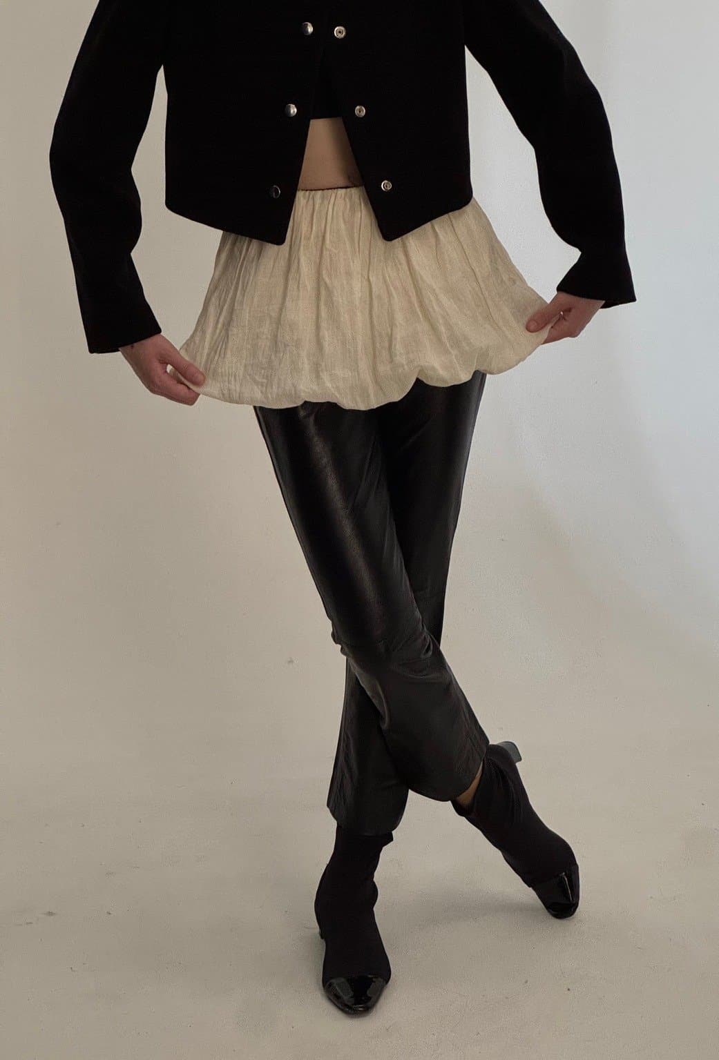 Model wearing a black cropped jacket, paired with shiny black pants and black boots in a slightly turned pose.