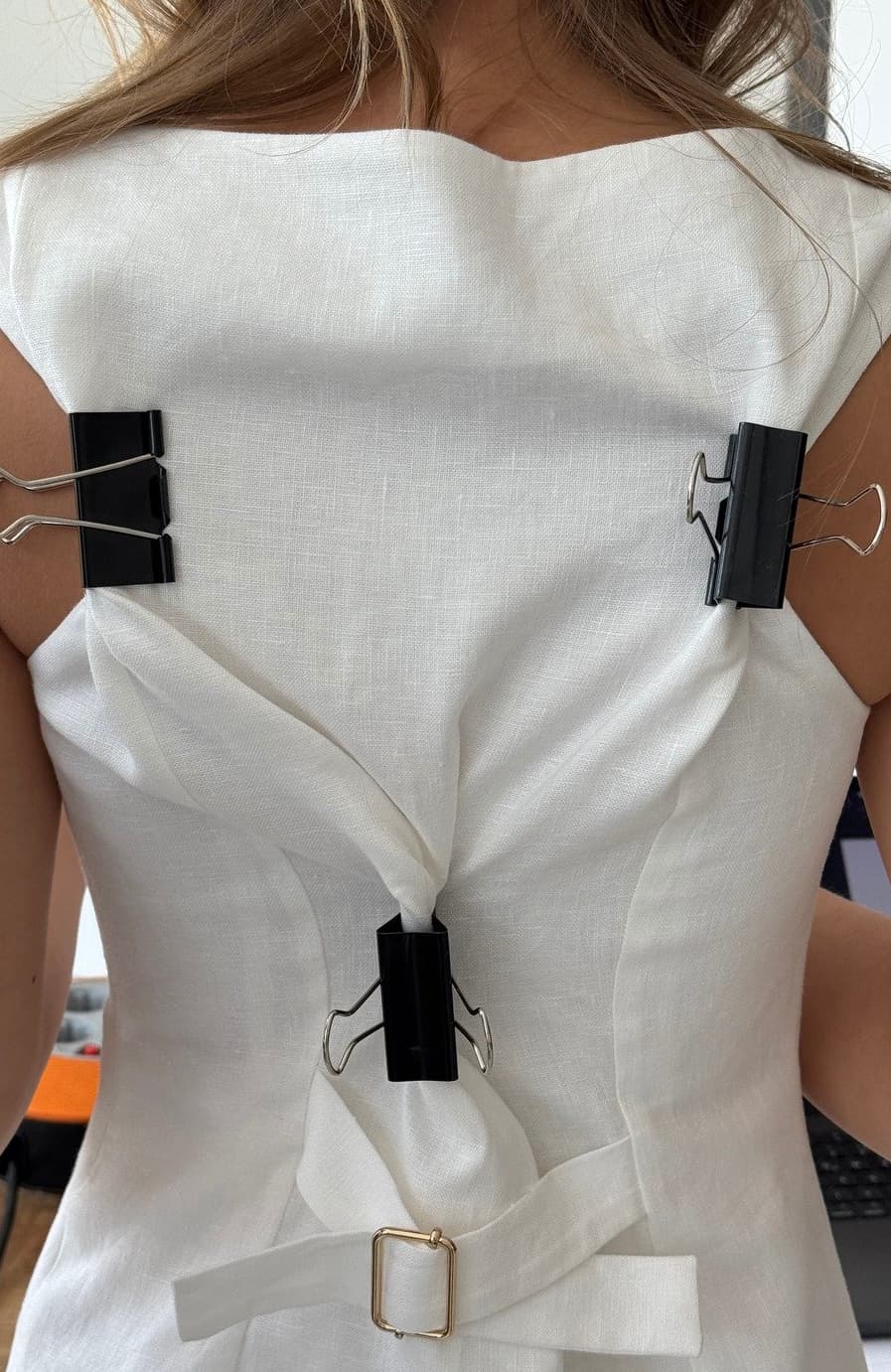 Close-up of a white structured garment on a model, cinched at the back with black binder clips during a fitting process.